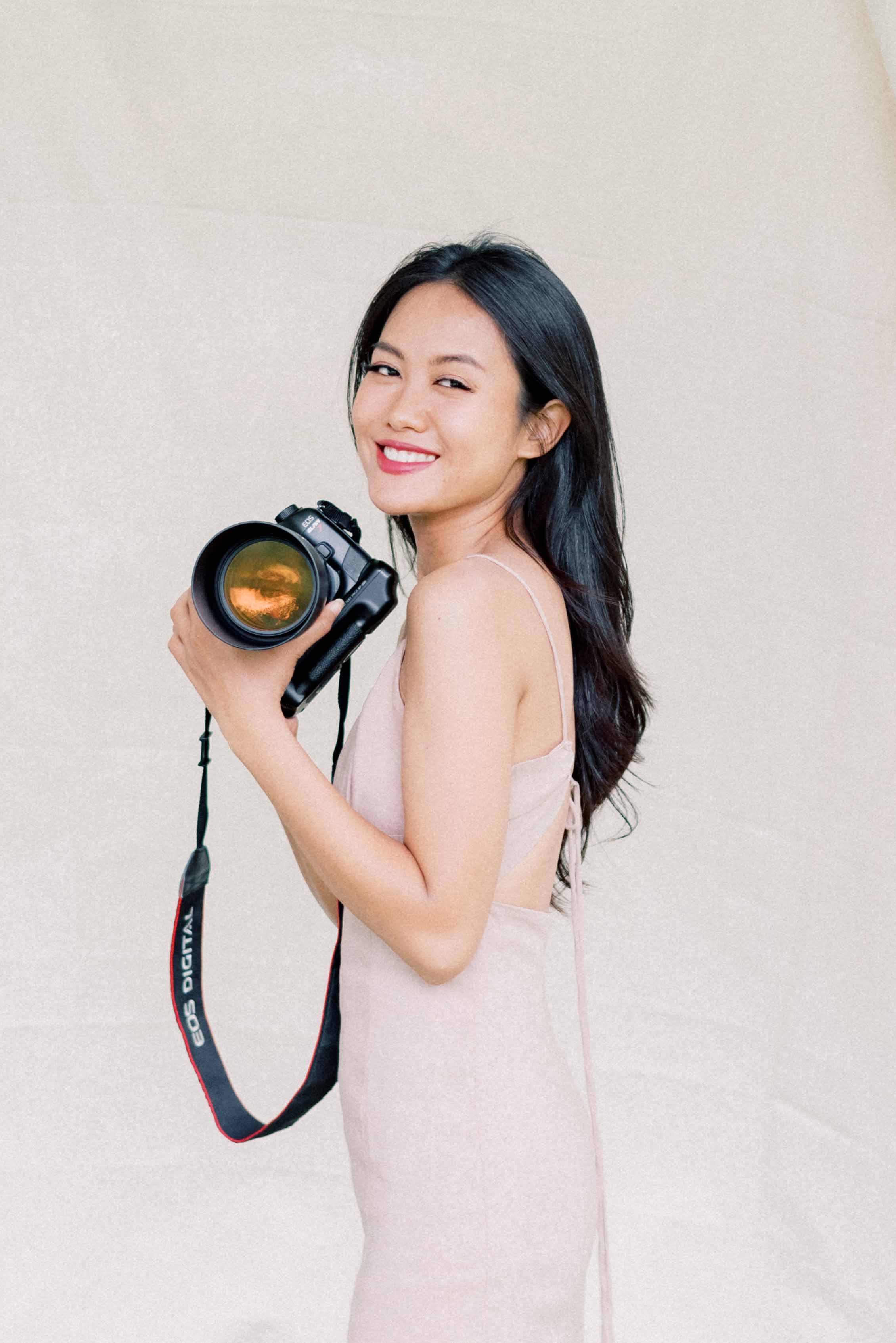 Kattariya May holding camera and smiling in front of white columns – branding portrait